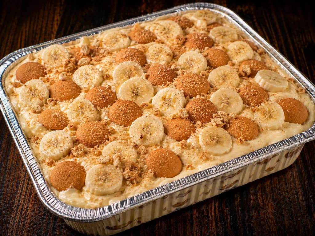 A full pan of banana pudding topped with overlapping banana slices, vanilla wafers, and crumbs